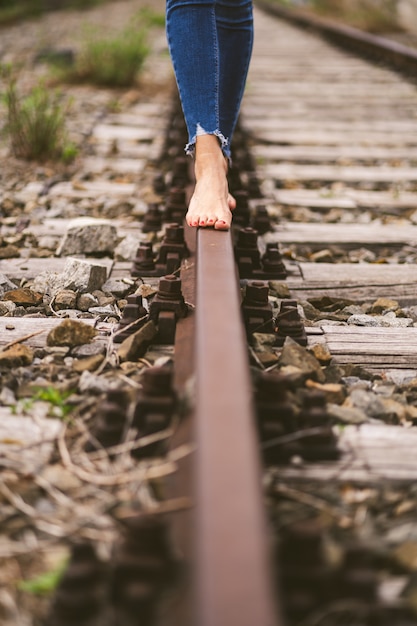 Disparo vertical de una mujer en jeans caminando descalzo por los rieles del tren