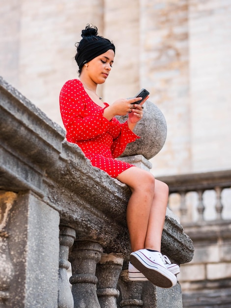 Disparo vertical de una mujer joven en vestido rojo con teléfono móvil al aire libre