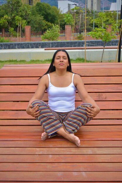 Disparo vertical de una mujer latina meditando en un banco de madera en el parque