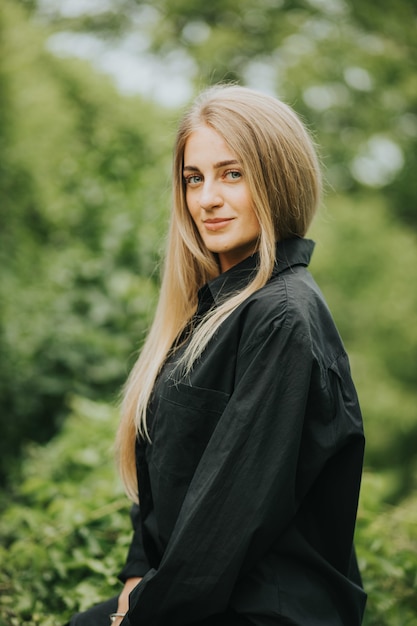 Disparo vertical de una mujer rubia caucásica de moda posando rodeada de vegetación