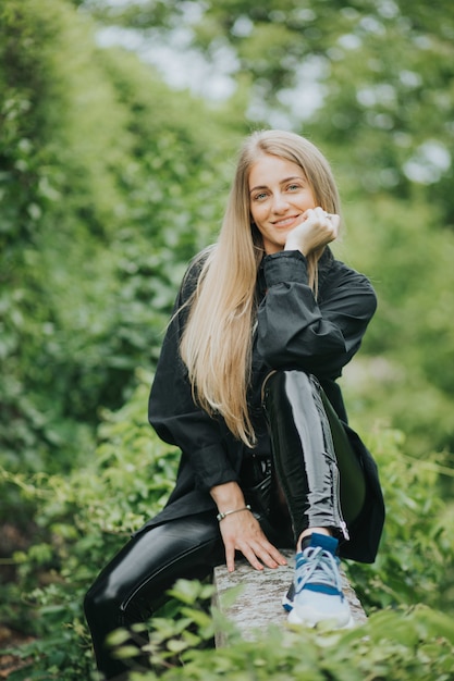 Disparo vertical de una mujer rubia caucásica de moda posando rodeada de vegetación