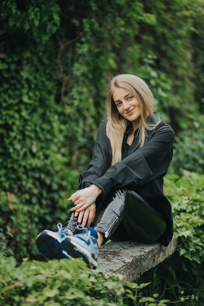 Disparo vertical de una mujer rubia caucásica de moda posando rodeada de vegetación