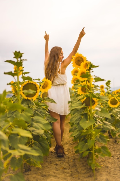 Disparo vertical de una mujer rubia joven alegre en un campo de girasol bajo la luz del sol
