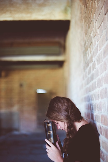 Foto gratuita un disparo vertical de una mujer sosteniendo la biblia cerca de su cabeza mientras rezaba