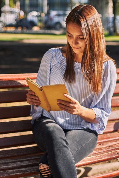 Disparo vertical de una niña con una camisa azul leyendo un libro en el banco