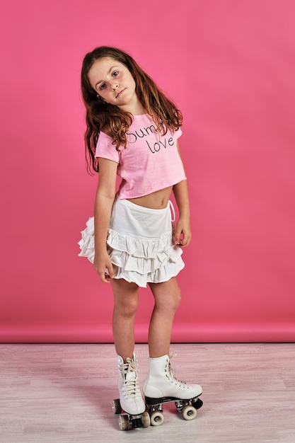 Disparo vertical de una niña posando en patines delante de una pared rosa
