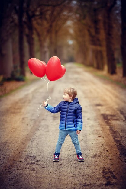 Disparo vertical de un niño sosteniendo globos en forma de corazón mientras está de pie sobre un camino de ripio
