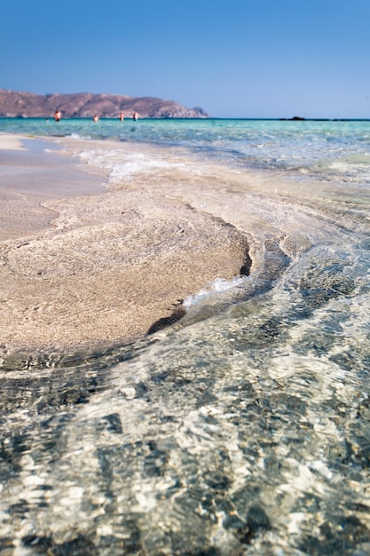 Disparo vertical de una orilla del mar bajo el cielo azul claro con gente nadando en la distancia