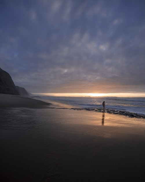 Disparo vertical de la orilla del mar en una hermosa puesta de sol con un joven caminando sobre el sealine