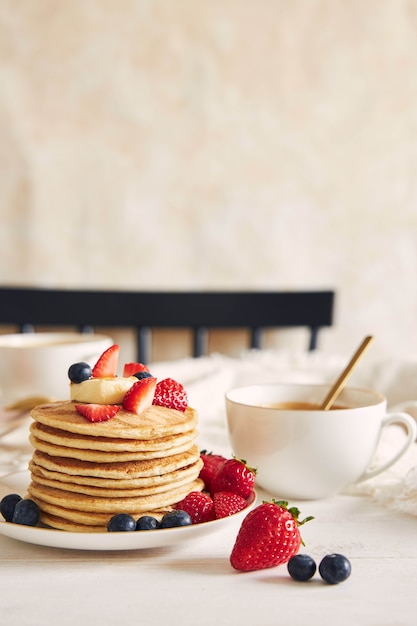 Disparo vertical de panqueques veganos con frutas coloridas ner un café y almíbar