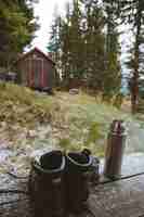 Foto gratuita disparo vertical de un par de botas y un matraz cerca de una cabaña de madera en el bosque en noruega