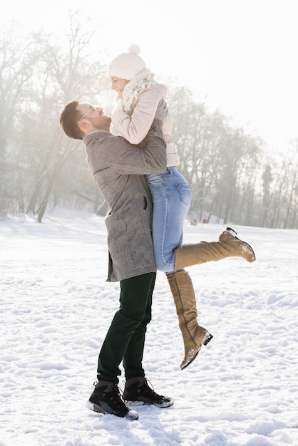 Disparo vertical de una pareja feliz disfrutando de la hermosa nieve en un frío día de invierno