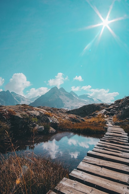 Disparo vertical de un pasaje de madera sobre un pequeño lago reflectante y una cordillera en el horizonte