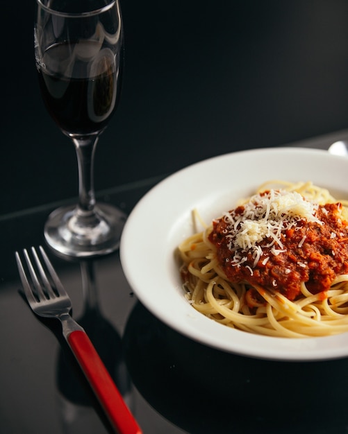 Foto gratuita disparo vertical de pasta con salsa en un recipiente sobre la mesa con una copa de vino tinto