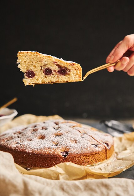 Disparo vertical de un pastel de cerezas con azúcar en polvo e ingredientes en el lado negro