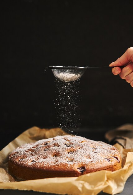 Disparo vertical de un pastel de cerezas con azúcar en polvo e ingredientes en el lado negro