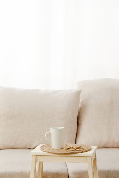 Disparo vertical de una pequeña mesa con una taza cerca de un sofá beige bajo las luces