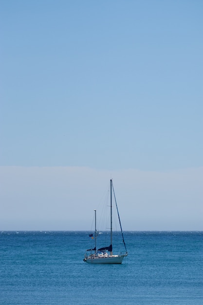 Disparo vertical de un pequeño barco navegando en el océano con un cielo azul claro