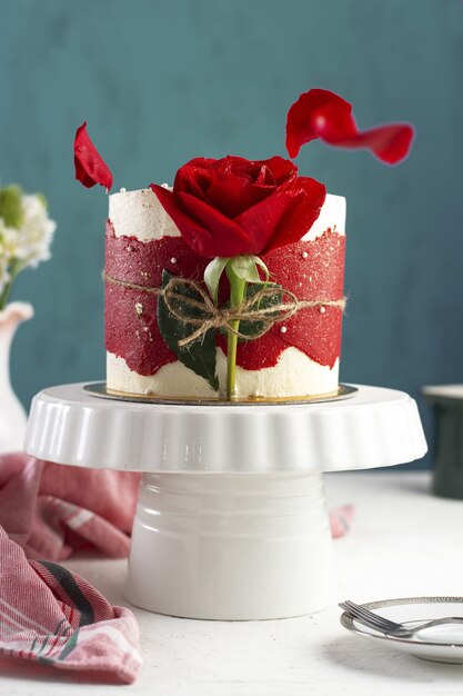 Disparo vertical de un pequeño pastel de fantasía con una rosa roja en una bandeja blanca