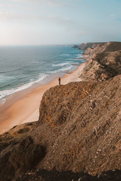 Disparo vertical de una persona en un acantilado mirando el hermoso océano en Algarve, Portugal