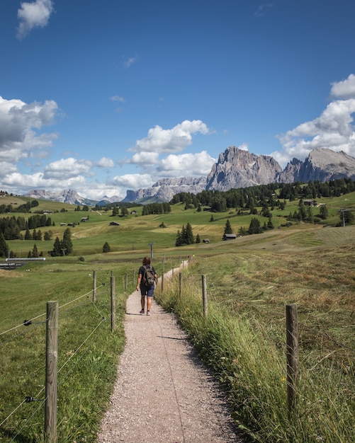 Disparo vertical de una persona caminando por un camino de tierra con la montaña Plattkofel