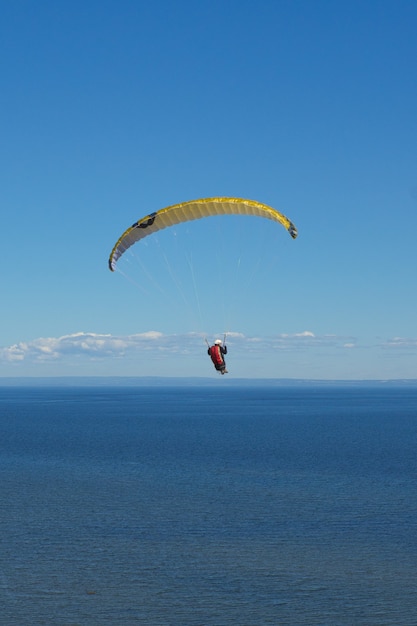 Disparo vertical de una persona volando en parapente sobre el mar bajo la luz del sol