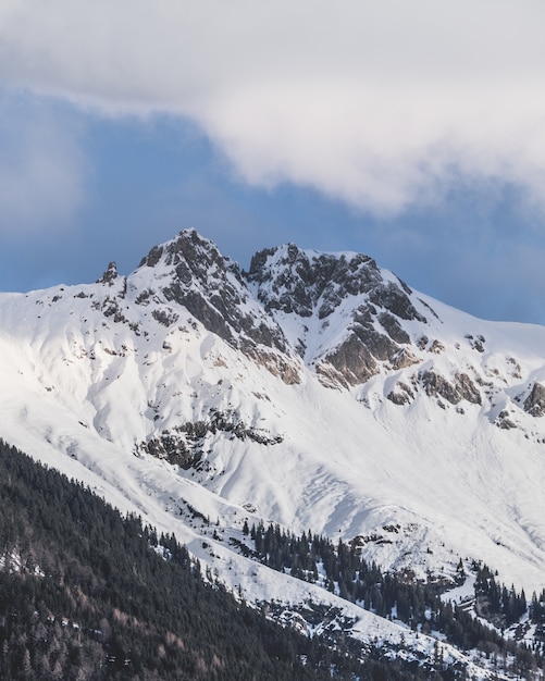 Disparo vertical de los picos nevados de las montañas bajo el cielo nublado