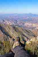 Foto gratuita disparo vertical de los pies de una persona sentada en la cima de una colina sobre un hermoso valle