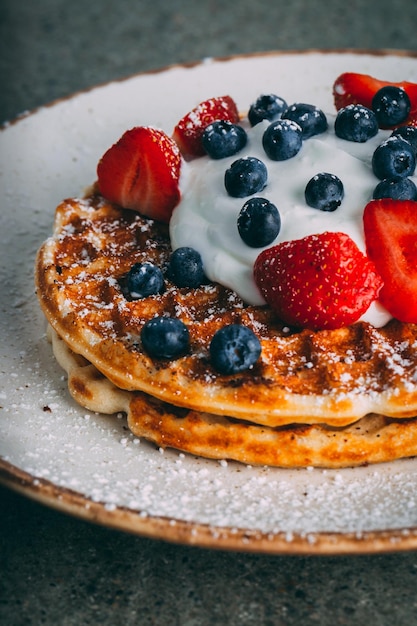 Foto gratuita disparo vertical de un plato con gofres gourmet con crema de fresas y arándanos