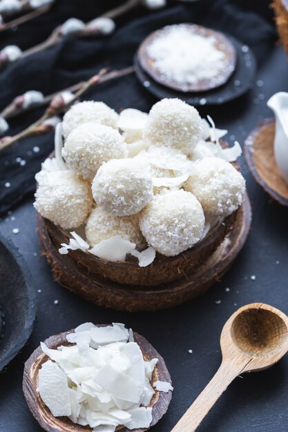 Disparo vertical de raffaello crudo en un cuenco de madera con trozos de coco y una cuchara de madera