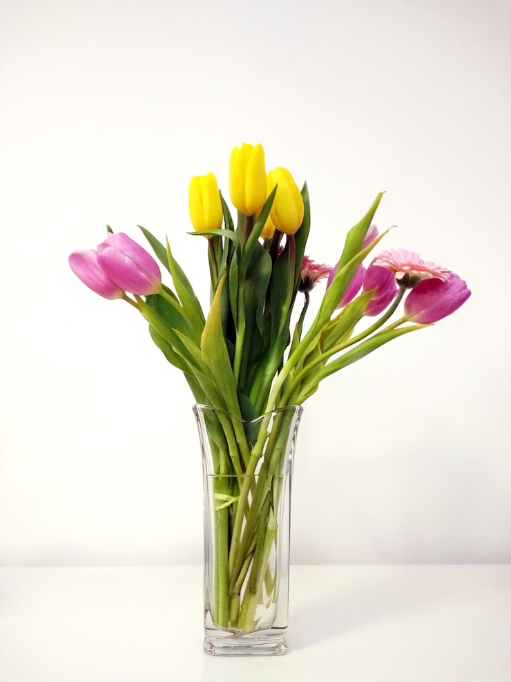 Foto gratuito disparo vertical de un ramo de tulipanes en un jarrón sobre la mesa bajo las luces