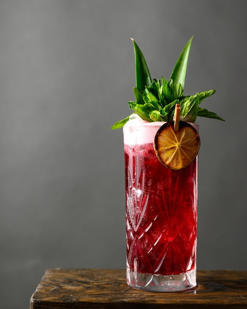 Disparo vertical de una refrescante bebida alcohólica roja con menta y limón seco sobre una mesa de madera