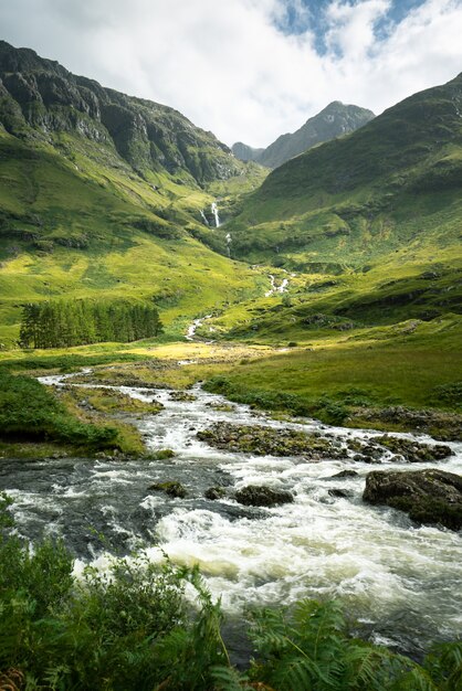 Disparo vertical de un río rodeado por montañas y prados en Escocia