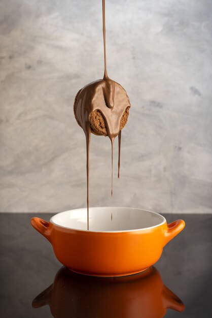 Disparo vertical de una sabrosa galleta cubierta de chocolate sobre un tazón de naranja