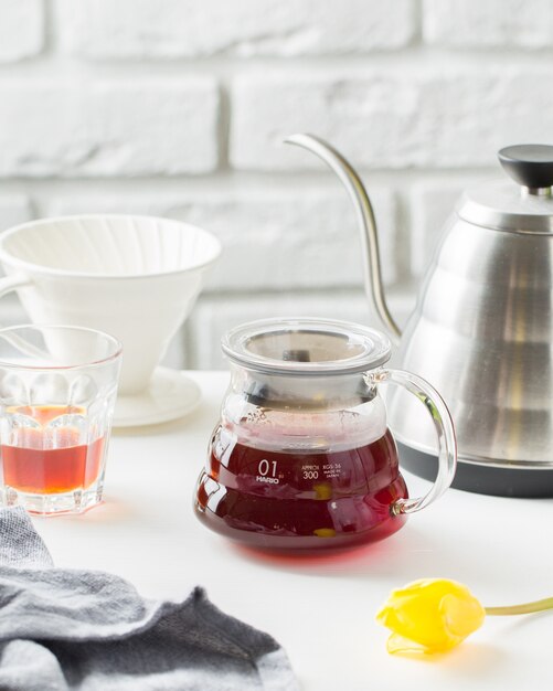 Disparo vertical selectivo de cerca de una jarra de vidrio para té cerca de una taza y hervidor de agua sobre una mesa