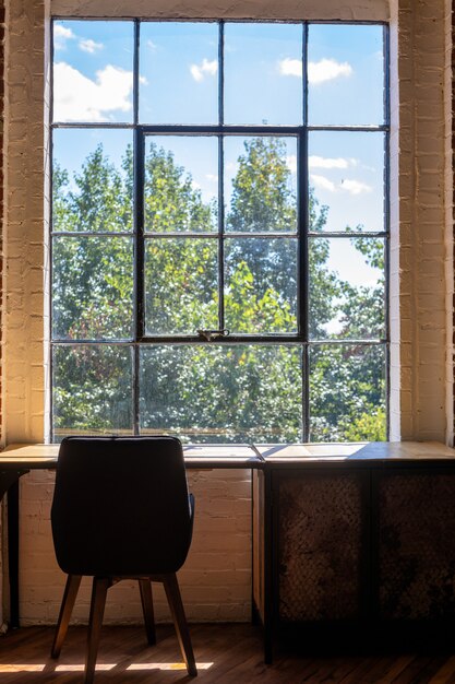 Disparo vertical de una silla y un escritorio cerca de una ventana grande con una vista increíble de vegetación afuera