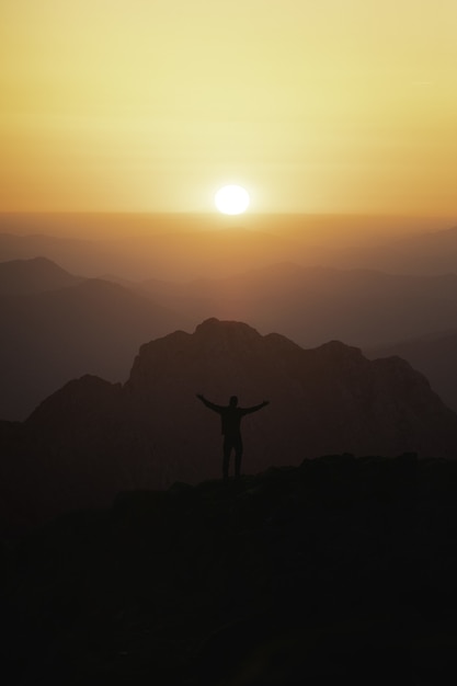 Foto gratuita disparo vertical de la silueta de un turista masculino en la cima de la montaña mirando la puesta de sol