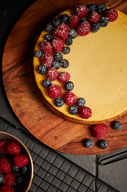 Disparo vertical de una tarta de queso con bayas en la parte superior sobre una placa de madera con bayas en el lateral