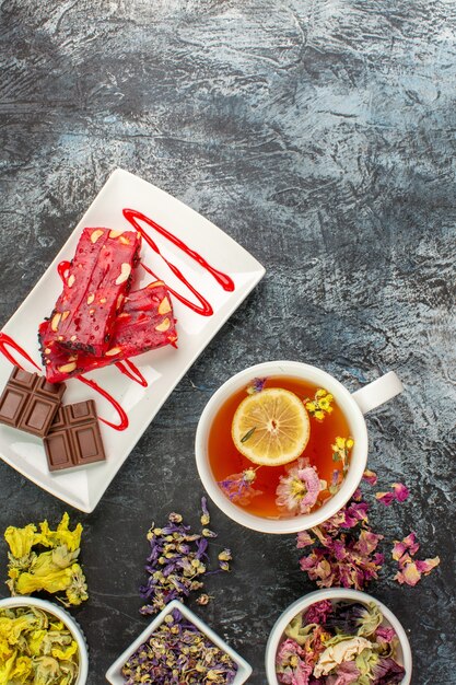 Disparo vertical de una taza de té de hierbas con flores secas y un plato de chocolate sobre suelo gris