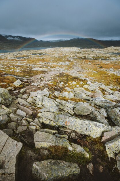 Disparo vertical de tierra con una gran cantidad de formaciones rocosas y el arco iris de fondo en Finse, Noruega