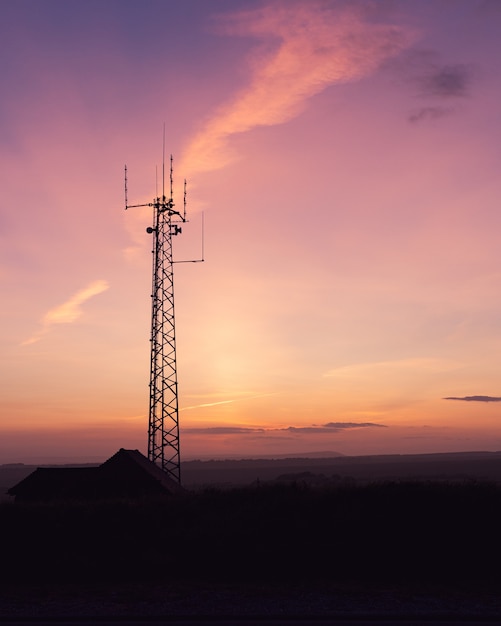 Foto gratuita disparo vertical de una torre de telecomunicaciones en un campo bajo el impresionante cielo, perfecto para papel tapiz