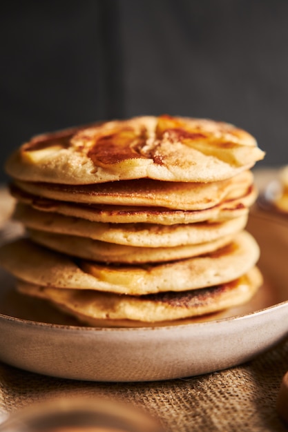 Disparo vertical de tortitas de manzana en un plato sobre un mantel marrón con una pared negra