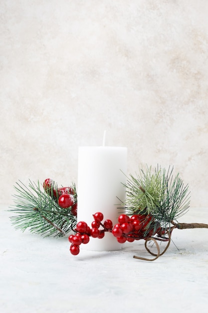 Disparo vertical de una vela blanca rodeada de acebos de Navidad y hojas sobre una superficie de mármol blanco