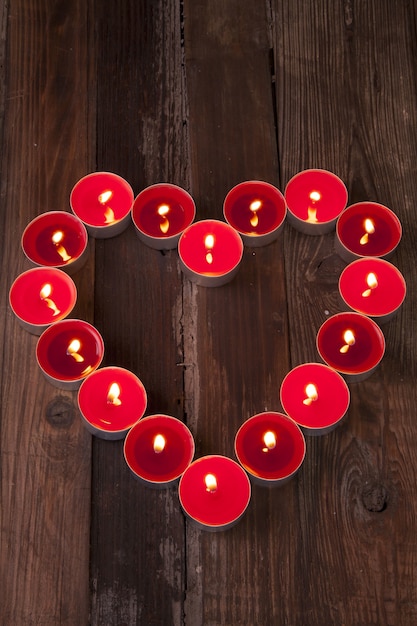 Foto gratuita disparo vertical de velas de té encendidas y rojas con forma de corazón sobre una superficie de madera