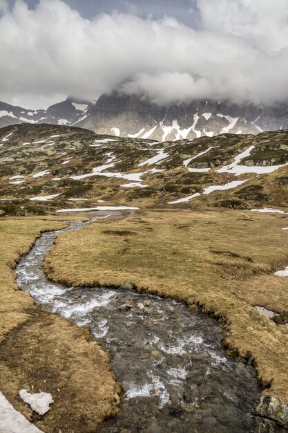Disparo vertical de una vista del paisaje cubierto de nieve con un río de montaña que fluye fresco