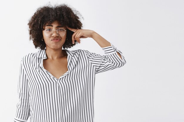 dispelido molesto mujer guapa hablando de un compañero de trabajo extraño y extraño moviendo el dedo cerca de la sien sonriendo y frunciendo el ceño por no le gusta pensar que está loco