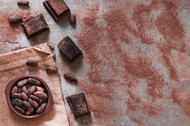 Dispersión de cacao en polvo con trozos de chocolate y tazón de frijoles de cacao