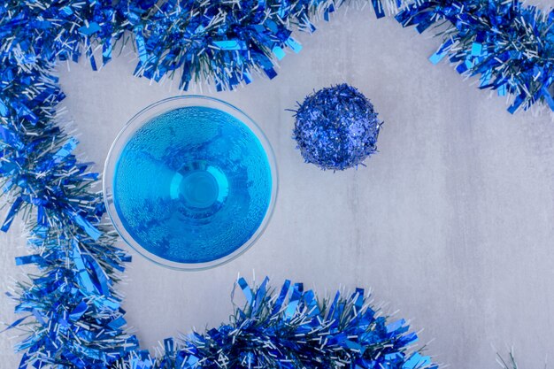 Disposición de copa de cóctel y adornos navideños azules sobre fondo blanco.