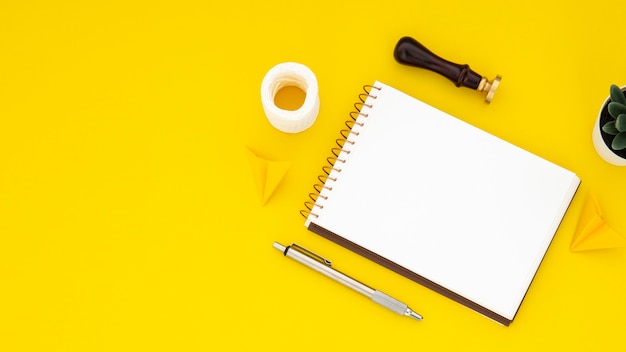 Disposición de elementos de escritorio con cuaderno vacío sobre fondo amarillo