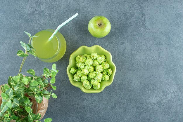 Disposición estética de tazón de palomitas de maíz, vaso de jugo de manzana, una sola manzana y un wase envuelto con una planta decorativa sobre fondo de mármol. Foto de alta calidad